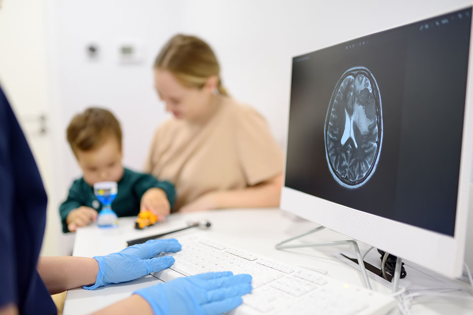 Toddler with Autism in the background, computer with brain scan in the foreground